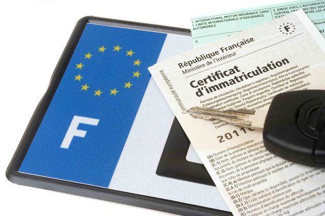 Un professionnel en concession consulte une interface SIV avec dossiers de carte grise sur le bureau