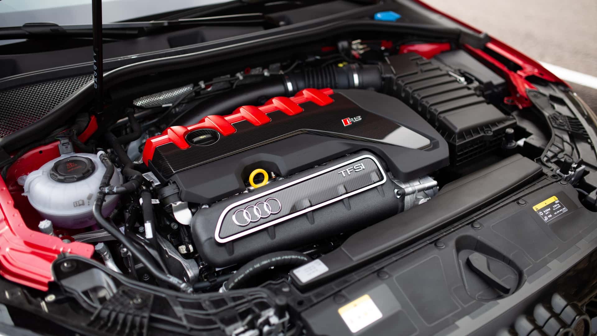 Audi RS3 Sportback gris Nardo en trois-quarts avant sur route de montagne, capot entrouvert sur le cinq-cylindres 2.5 TFSI