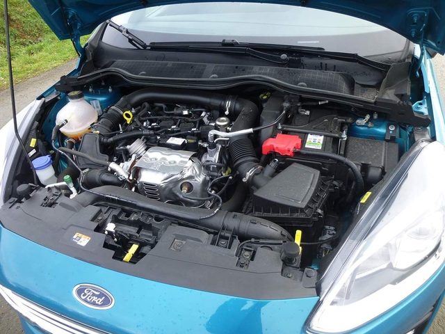 Vue plongée sur le moteur trois-cylindres 1.0 EcoBoost d'une Ford Fiesta, capot ouvert dans un atelier en lumière naturelle