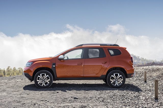Un Dacia Duster II gris en vue trois quarts avant roule sur une route française, garde au sol mise en valeur