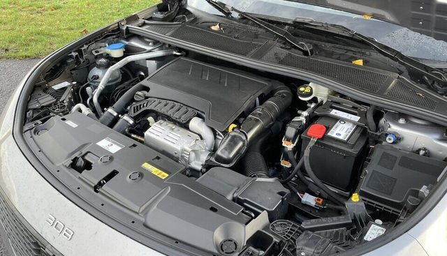 Peugeot 208 d'occasion capot ouvert sur un parking de vendeur, carnet d'entretien posé sur l'aile, vue trois-quarts avant