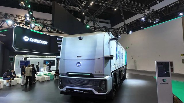 Un camion lourd électrique moderne circule sur une plateforme logistique avec des bornes de recharge en arrière-plan