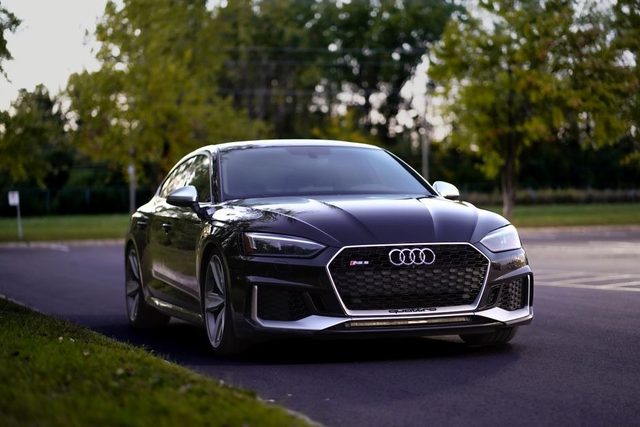 Une Audi RS noire stationnée en vue trois quarts avant sur une route française bordée d’arbres
